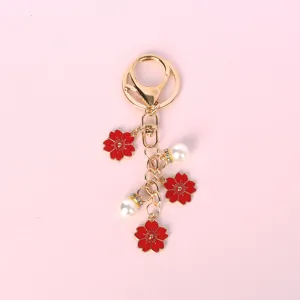 Detalle de flores de cerezo en esmalte rojo y perlas en un llavero de metal dorado