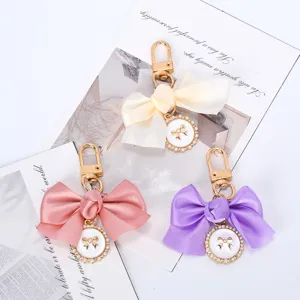 Detail of cute satin bow keychains with pearl charms in pink, purple, and cream.