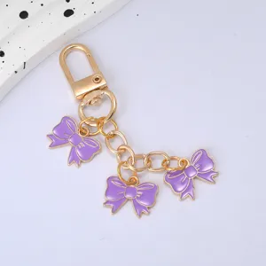 Detail showing three purple enamel bow charms on a gold-tone keychain for bags
