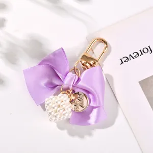 Close-up of elegant purple ribbon bow keychain with pearl cube and gold charm detail