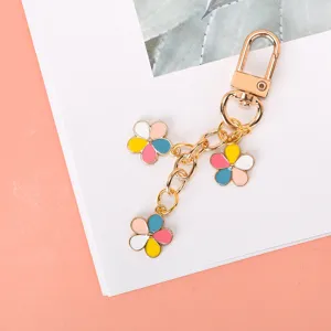 Close-up of gold-tone keychain with three colorful enamel flowers on a white surface.