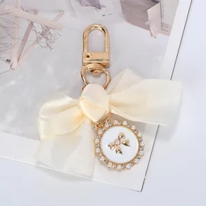 Close-up of elegant cream ribbon bow keychain with pearl and rhinestone circular charm