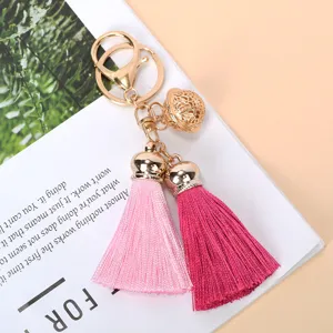 Close-up detail of a fashion keychain featuring double tassels and a gold bell charm.