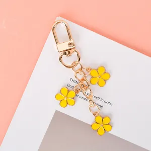 Detail of yellow floral enamel keychain with three charms on a gold-plated link chain.