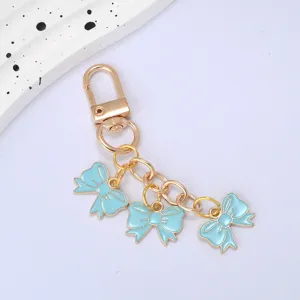 Detailed view of three light blue enamel bow pendants on a gold-colored metal keychain