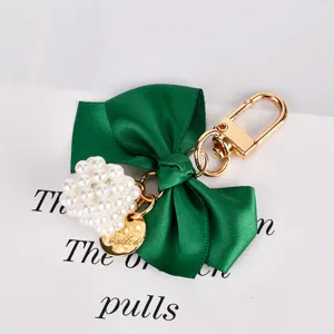 Close-up of green ribbon bow keychain with white pearl cube and gold clasp detail