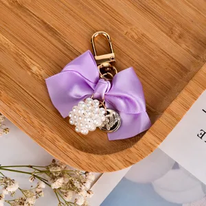 Close-up of purple ribbon bow keychain with pearl cluster and gold clip on bamboo tray