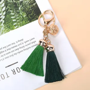 Detail view of a gold-toned keychain featuring a hollow bell and two green tassels