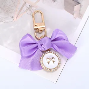 Detail of a purple ribbon bow keychain featuring a pearl-encrusted pendant.