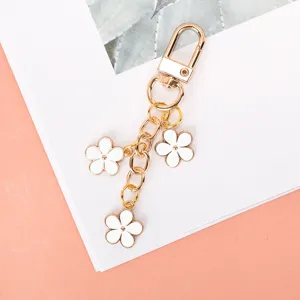 Detailed macro view of a gold-plated keychain featuring three white enamel flower charms