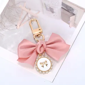 Close-up of the elegant pink satin bow keychain with a pearl-rimmed enamel charm