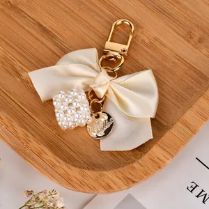 Detailed view of cream ribbon bow keychain with pearl cube charm and gold clasp