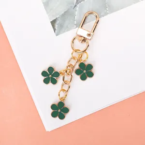 Close-up of golden keychain with three green enamel flower charms on white background.
