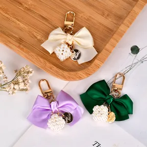 Elegant ribbon bow keychains featuring pearl cubes and golden metal lobster clasps