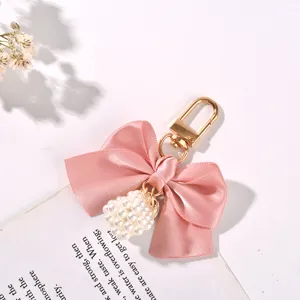 Close-up of a sweet pink ribbon bow keychain featuring a delicate white pearl cube.