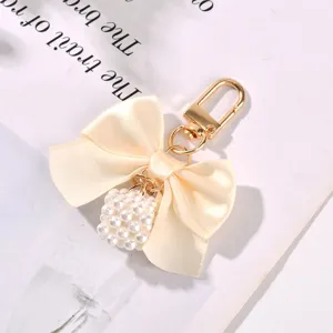 Elegant cream satin bow keychain with a pearl cube charm and gold metal clasp