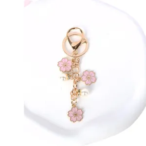 Elegante llavero de flor de cerezo rosa con acabado dorado y detalles de perlas blancas