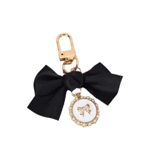 Elegant black ribbon bow keychain featuring a pearl-lined white circular charm