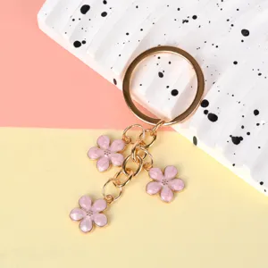 Gold metal keychain with three pink enamel cherry blossom charms on a colorful background