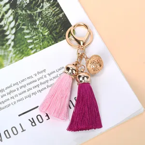Macro detail of golden hollow bell charm and vibrant pink and purple tassels on keychain