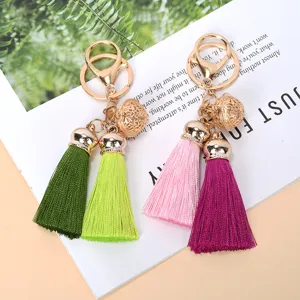 Detailed view of colorful tassel and hollow gold bell keychains for bags.