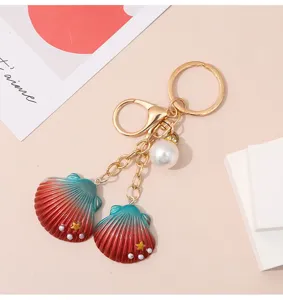 Detail of teal-to-red gradient resin shell keychain with elegant white faux pearl