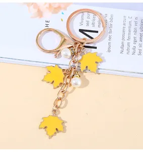 Detailed view of gold metal keychain featuring yellow maple leaves and elegant pearls.