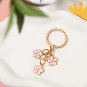Detail of a gold-toned keychain featuring three delicate pink enamel flower charms.