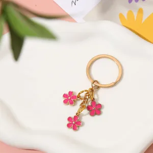 Macro detail of a gold metal keychain with three pink enamel flower charms on a tray.