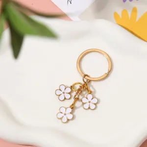 Detailed view of gold-tone keychain with three white enamel flower charms