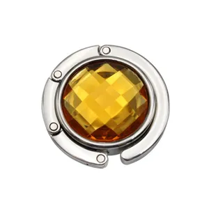 Detailed view of a circular foldable metal bag hook featuring a large amber gemstone center.