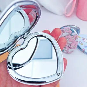 Close-up of a heart-shaped silver folding compact mirror held in hand for portable makeup