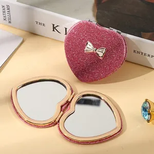Pink glittery heart-shaped compact mirror with gold bow decoration, double-sided folding