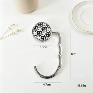 Close-up of foldable metal bag hook with checkerboard smiley face and dimensions