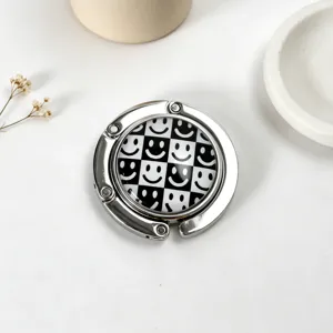 Close-up of portable foldable metal handbag hook with black and white smiley checkerboard design