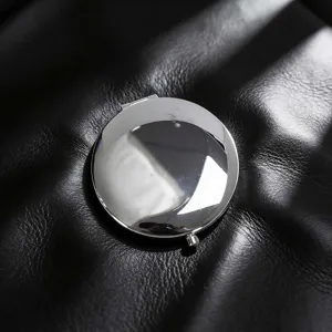 Close-up of a polished chrome folding makeup mirror on a textured black leather surface