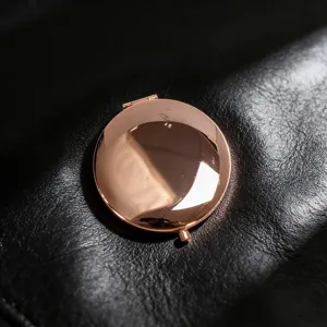 Detail view of a polished rose gold circular portable makeup mirror on black leather
