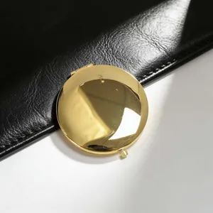Close-up of a gold-colored portable circular folding compact mirror on leather