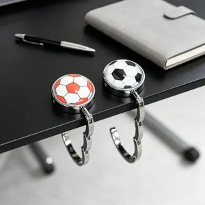 Zwei faltbare Metall-Handtaschenhalter mit Fußball-Design an einer Schreibtischkante.