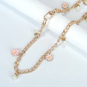Détail d'une chaîne de sac dorée avec des fleurs de marguerite roses et perles