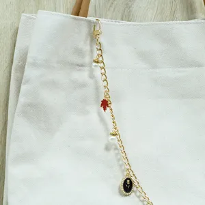 Élégante chaîne de sac en métal doré avec des breloques feuille et perle sur un sac en toile