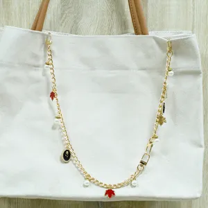 Gros plan d'une chaîne de sac dorée avec des perles et des breloques feuilles d'érable.