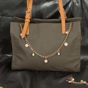 Détail de chaîne de sac dorée avec fleurs roses et perles sur un sac à main en cuir