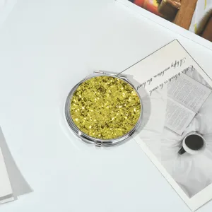 Gros plan d'un miroir de poche rond en métal avec un couvercle à paillettes dorées