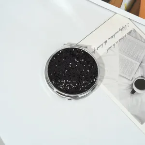 Vue détaillée d'un miroir de maquillage rond portable à paillettes noires sur table