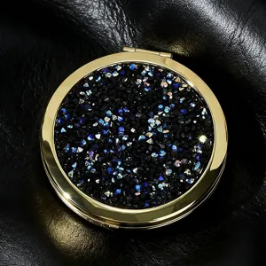 Detailed close-up of circular gold compact mirror with sparkling black and blue glitter.
