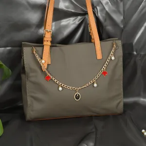 Détail d'une chaîne décorative dorée pour sac à main avec perles et breloques en forme de feuille