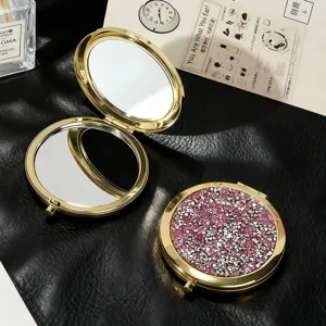 Detailed view of pink glitter texture on a gold-toned circular folding makeup mirror.