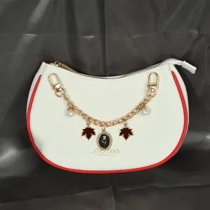Détail d'un sac blanc avec chaîne à fleurs dorée et breloque en forme de rose.