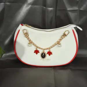 Détail d'un sac à main semi-circulaire blanc avec chaîne dorée à fleurs et bords rouges